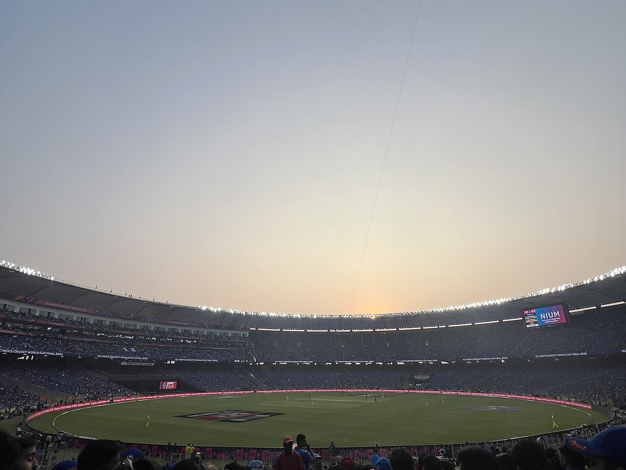 FairPlay Gujarat Cricket Stadium: a floodlit stadium bowl at dusk with a bat, ball and helmet in front